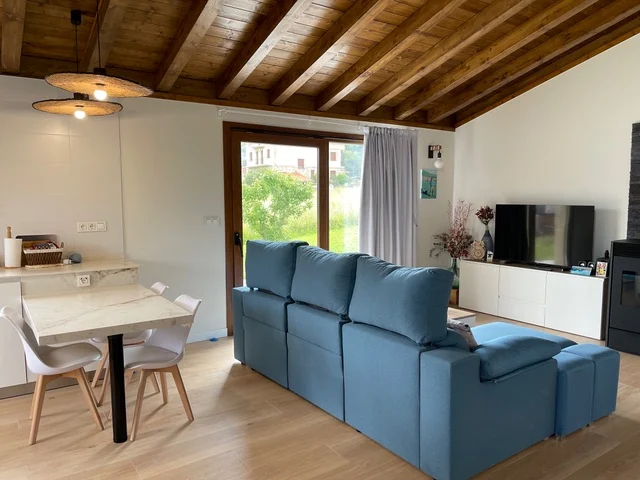 Salón con sofá azul y comedor bajo un techo de vigas de madera